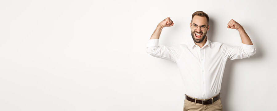 Successful manager flex biceps, showing muscles and looking confident, standing over white background