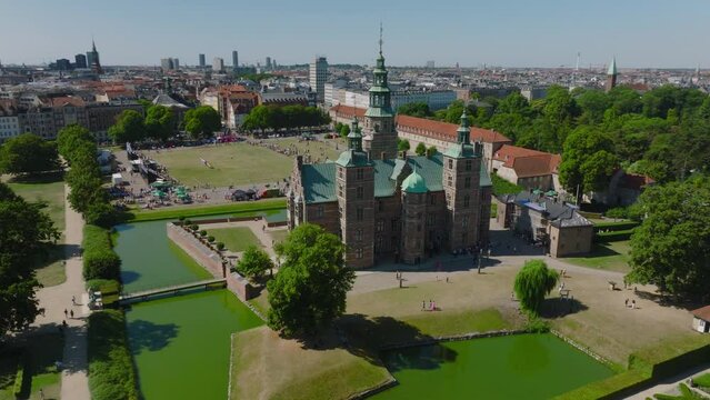 Circular aerial footage of Rosenborg castle in Kongens Have park on sunny day. People sightseeing and watching football match. Copenhagen, Denmark