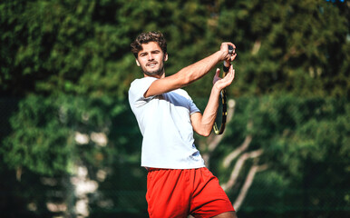 A handsome young Caucasian tennis player executes a forehand stroke with his racket, and plays on...