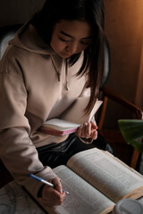 Shot of young asian female student sitting at table and writing on notebook. Young female student studying in cafe.