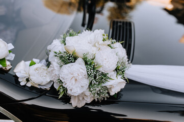 Fresh, paper white flowers, decorations with a ribbon on a black car hanging close-up. wedding photography.