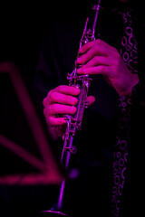 A musician with a clarinet next to a music stand illuminated with purple light