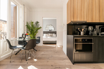 Studio apartment with an open kitchen with black base units and a round glass dining table next to a balcony