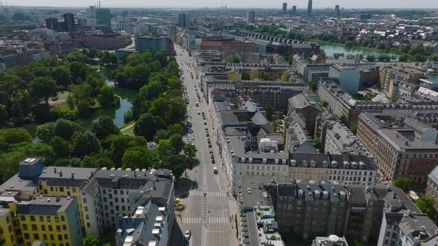 Forwards fly above buildings in urban borough. Tilt up reveal cityscape. Blocks of townhouses, streets and lakes surrounded by green vegetation. Copenhagen, Denmark
