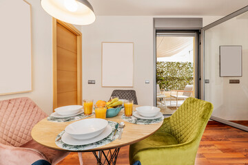 Living room of an apartment with round wooden dining table with breakfast service with fruits and glasses with orange juice