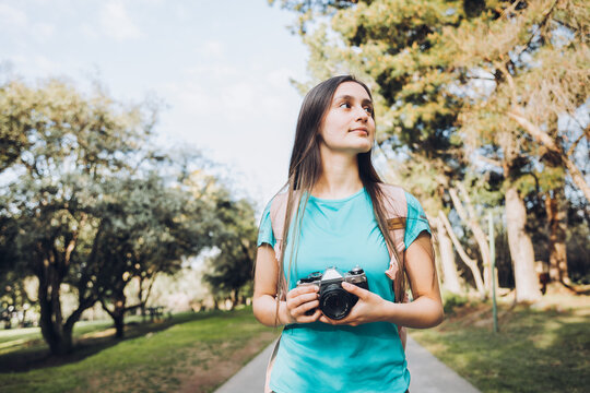Young tourist woman traveler, wearing turquoise t shirt and a backpack, taking photos while walking in the park.