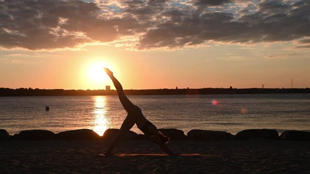 Slow motion video of a young woman doing yoga workout on Baltic sea coastline during subset