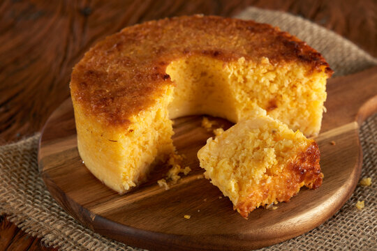 Homemade round cake made of green corn and cheese, known as "Pamonha Cake". Typical Brazilian food of Festa Junina(june festival) with a piece cut on a round wooden board on a rustic wooden table