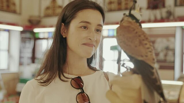 Woman tourist admiring a holding hooded Falcon at Falcon Sou in Doha Qatar. Market selling live falcon birds and falconry equipment in the center of Doha. 

