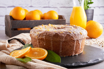 Traditional Brazilian orange cake with orange and lemon zest topping on a stone table and white brick rustic background. Oranges inside a rustic wooden crate. Orange juice and orange slices