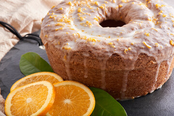 Traditional Brazilian orange cake with orange and lemon zest topping on a stone table and white brick rustic background. Orange slices and orange leaves on the side