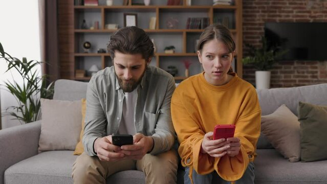 Young couple with smartphones ignoring each other. Man and woman using smartphones after argument sitting on a couch at home. Communication problems and social network addiction. Family conflict.