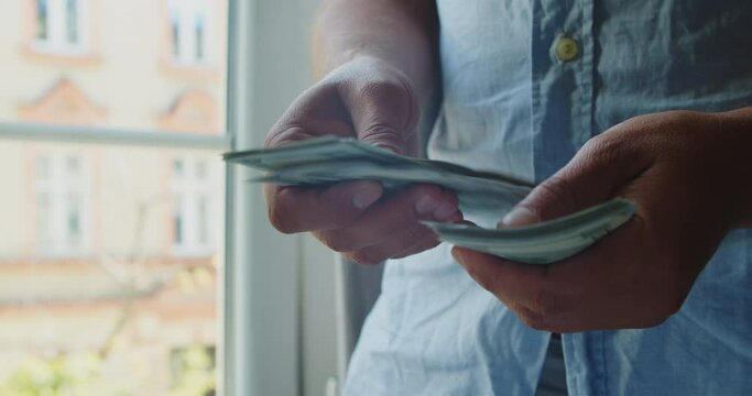 A young man redraws money, a salary in the hands of one hundred dolor bills. close-up of male hands counting a stack of hundred-dollar US banknotes.