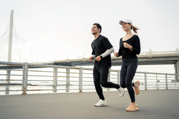 A sporty couple running down the street, fitness training running in sneakers. They use a fitness watch on their arm.