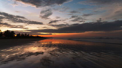 Vivid dawn colors at a tropical beach and sky clouds reflection on wet sand, shown in Chiriqui, Panama.