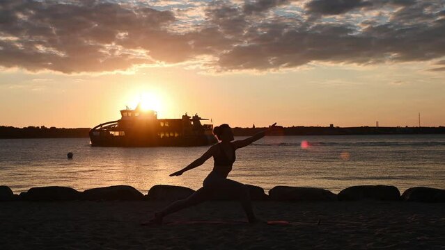 Slow motion video of a young woman doing yoga workout on Baltic sea coastline during subset