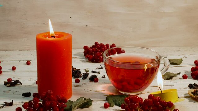 A cup with red tea and burning candles on a white wooden table. Natural tea from the red viburnum berry on wooden rural boards. Naturopathy healing infusion. Natural antioxidant drink made from red