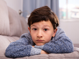 Unhappy schoolboy sitting at sofa and thoughtful about trouble with parents
