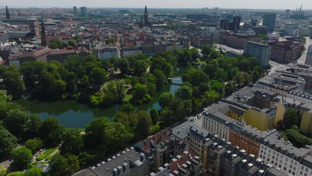 Aerial cinematic shot of Orstedsparken. Public park with lake and trees. Revealing cityscape on sunny day. Copenhagen, Denmark