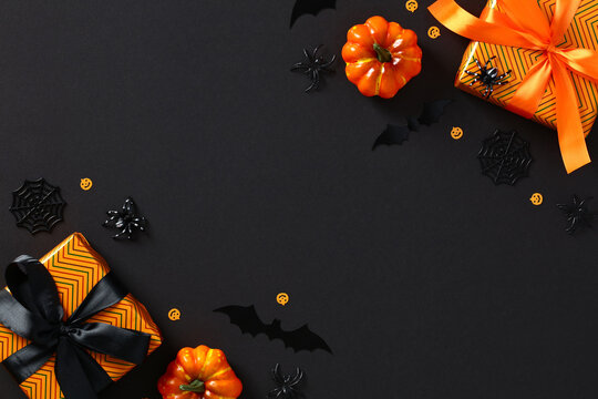 Happy Halloween holiday composition. Flat lay orange gift boxes with ribbon bow, pumpkins, bats, spiders on dark black table. Spooky, scary Halloween greeting card design.