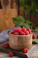 Bowl of fresh ripe raspberries on wooden table against blurred background