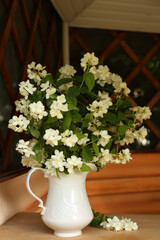 Fototapeta na wymiar Bouquet of beautiful jasmine flowers in vase on wooden table indoors