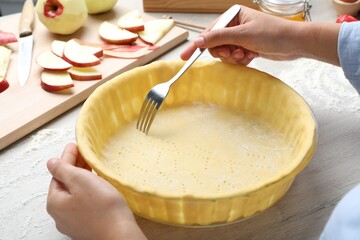 Woman making holes in raw dough with fork at white wooden table, closeup. Baking apple pie