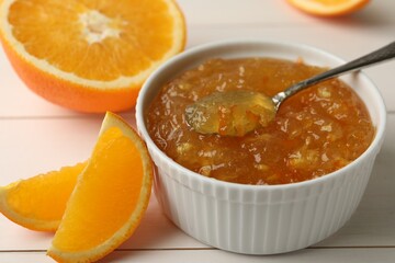 Delicious orange marmalade in bowl with spoon on white wooden table, closeup