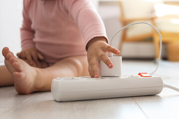 Fototapeta premium Cute baby playing with charger and power strip on floor at home, closeup. Dangerous situation