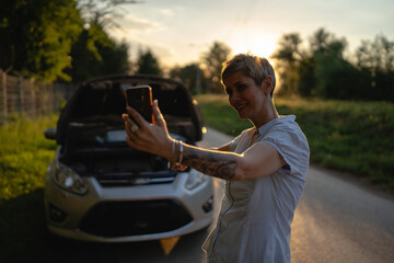 one woman mature female standing on the road in the evening sunset by the broken vehicle car...