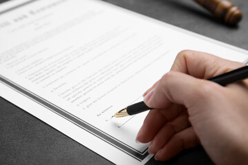 Woman signing last will and testament at grey table, closeup