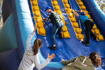 Group of enthusiastic men and women passing obstacles and having fun on inflatable arena at...
