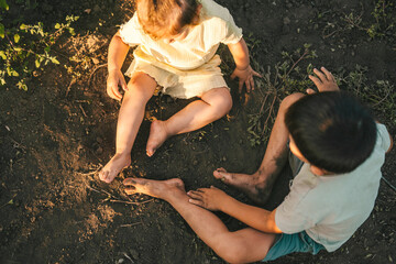 Top view of two dirty children resting on the ground after helping their parents work in the...