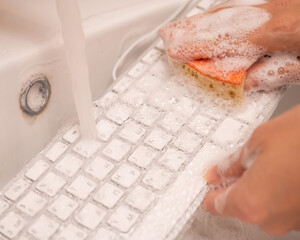 Fototapeta premium Woman washing white computer keyboard with a sponge with foam.