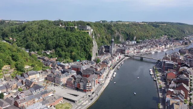Scenic summer view of Dinant cityscape on banks of river Meuse overlooking Collegiate Church of Notre Dame and fortified Citadel on top of cliff overgrown with green trees, Namur province, Belgium