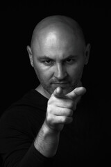 Bald man with a beard, on a dark background, points his index finger at the camera. Motivation for action, motivation. Vertical photo.