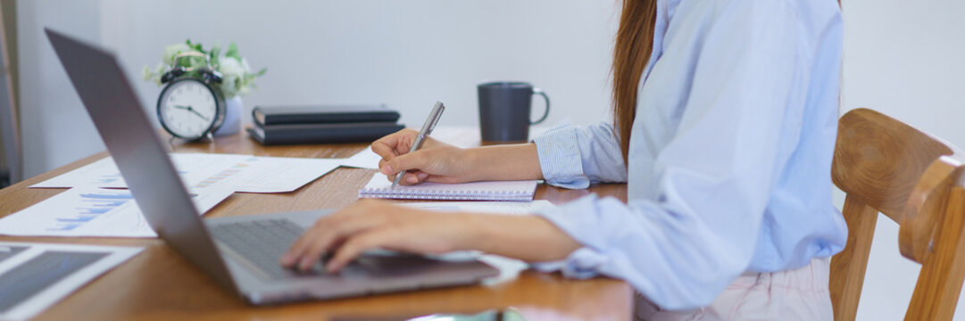 Business at home concept, Businesswoman is reading marketing plan data on laptop and taking notes