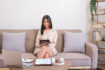 Relaxation lifestyle concept, Asian woman sitting on sofa and writing on tablet to working at home