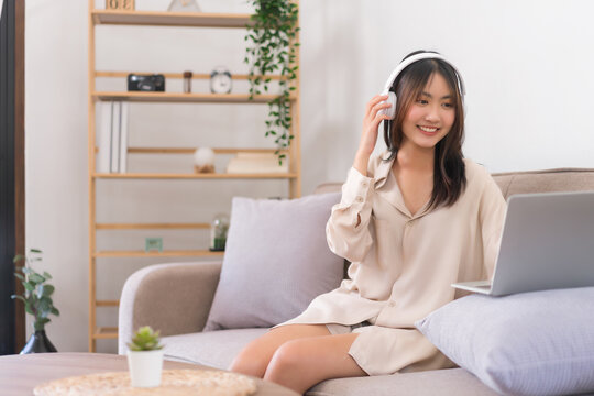 Concept of activity in living room, Asian woman is listening music and chat with friend on laptop