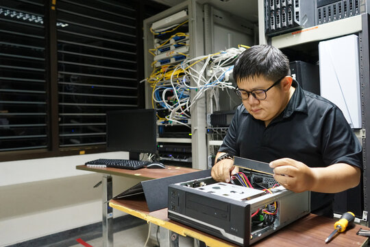 Young concentrated technician fixing a computer and changing wires at server room.