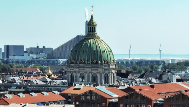 Beautiful large dome of Frederiks Kirke against zoomed background. Power plant and wind farm on seashore. Copenhagen, Denmark