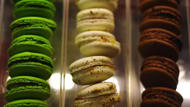 Closeup scan of lime, pistachio, and chocolate macarons aligned in glass case 