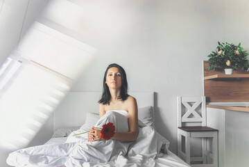 beautiful young woman sitting in bed in the morning in a romantic setting with a flower