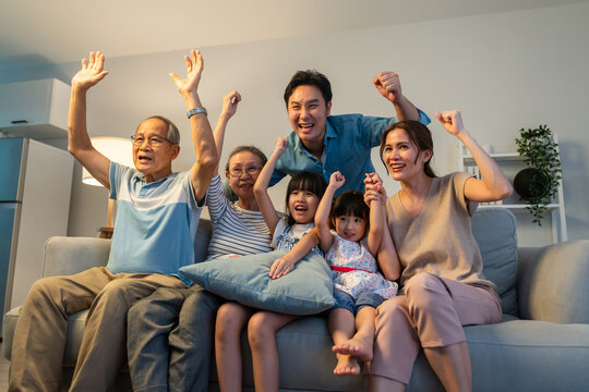 Asian family cheering and watching football on television at home.