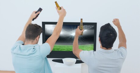 Composition of two male sports fans watching sports stadium on tv