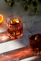 Photo composition of two Negroni glass cocktail with sun light and shadow and orange