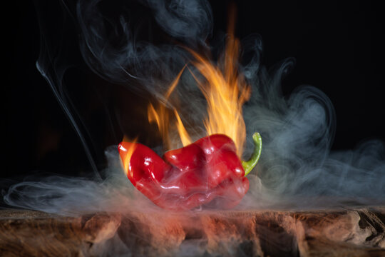 A hot chilli is surrounded by fire and smoke. It's a habanero. The background is black.