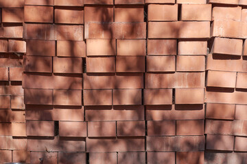 There is a pile of red bricks in the yard. A sunlight-lit shadow from the leaves of a tree falls on a pile of bricks.