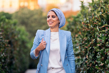 Portrait of a muslim woman standing among large bushes on a pathway looking at camera