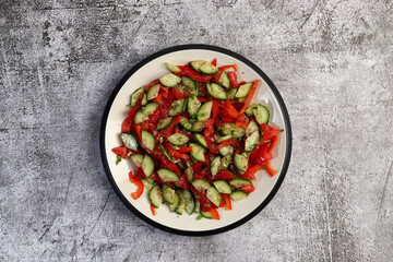 Cucumbers, bell pepper and herbs fresh healthy salad  on a round plate on a dark gray background. Top view, flat lay